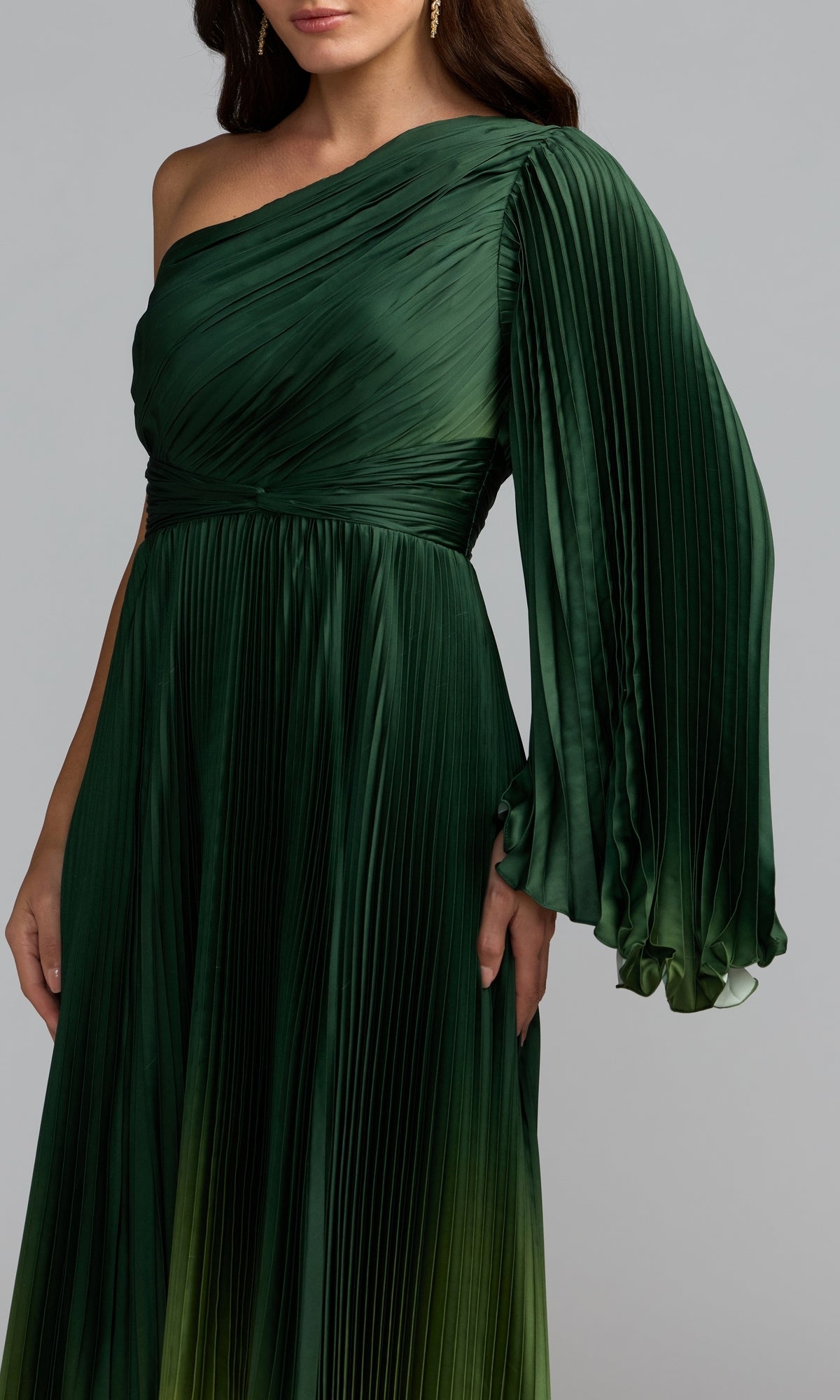 A woman wears the Mac Duggal 49903 One-Shoulder Ombre Formal Dress, featuring dark green pleated fabric, a long flowing sleeve, and a gradient hem. Only her torso is visible.
